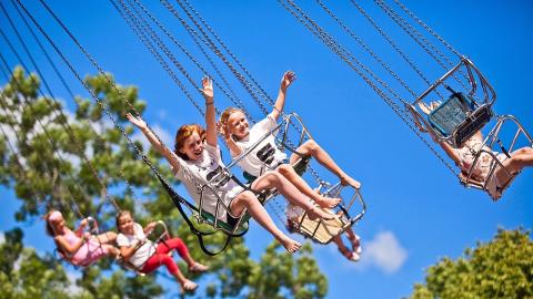 Barn åker karusell i luften med göra träd och blå himmel i bakgrunden