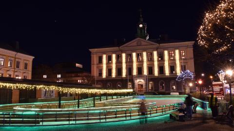 Upplyst skridskobana framför en upplyst ståtlig palatsliknande byggnad en vinterkväll