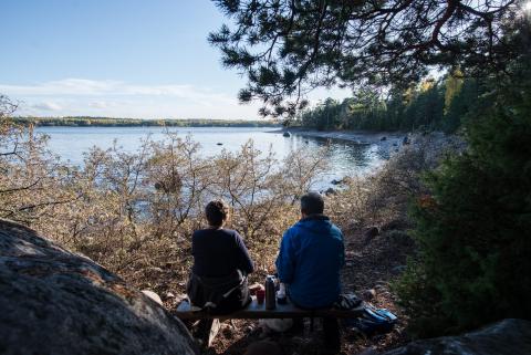 Ett par i förgrunden har picknick och tittar ut över en sjö en höstdag.