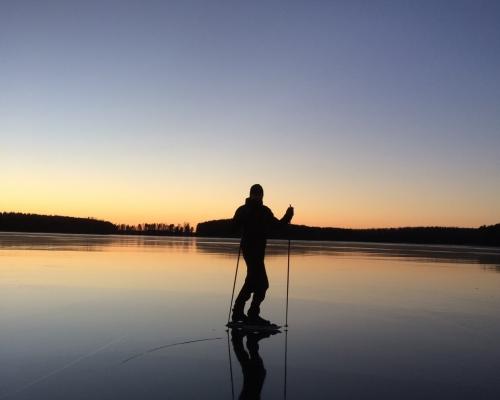 Man som åker långfärdsskridskor på Storsjön i solnedgång