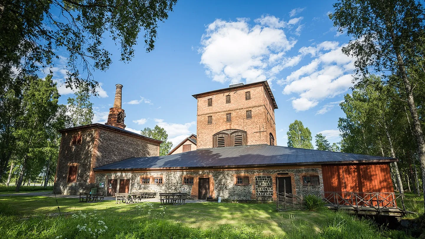 Stor tegelbyggnad inbäddad i grönskande glänta en fin sommardag 