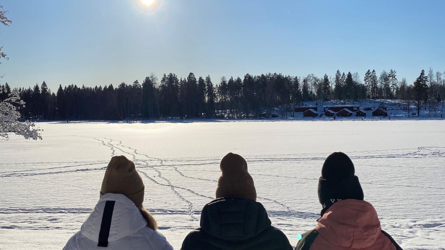 Tre personer njuter av vintersolen vid kanten av isbelagd Högbo sjön