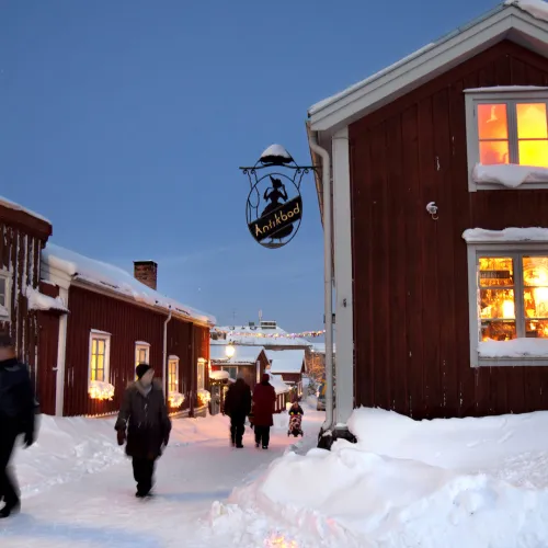 Gågata med massor av snö mellan röda hus en klar vinterkväll