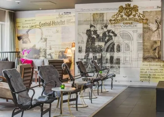 Hotell lobby med bord, stolar, kamin och ett konstverks om fondvägg