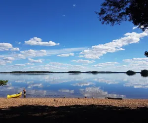 Kanot på fin strand på Sandön en dag med blå himmel och spegelblankt vatten