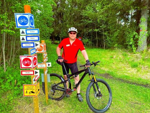 Dan Dannberg med cykel i skogen bredvid skyltar för cykelleder.