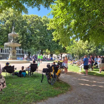 Folksamling i en park med gröna träd och en fontän
