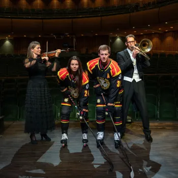 Hockeyspelare och violinister står på en scen inomhus