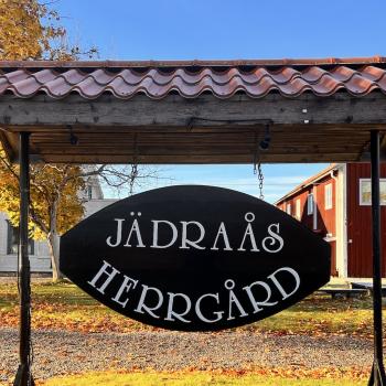 Stor skylt med texten Jädraås Herrgård med två byggnader i bakgrunden en fin dag i oktober