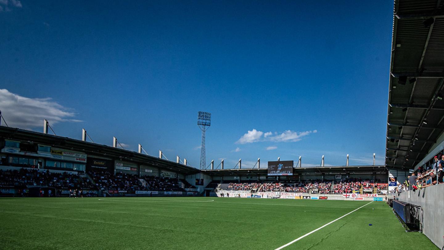 Fotbollsarenan Gavlevallen med en grön tom gräsmatta, publik på läktaren och blå himmel